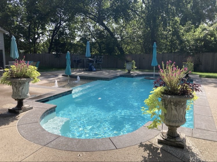 Kidney-shaped backyard pool with deck fountains and planted stone urns